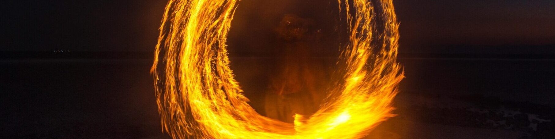 Captivating long exposure shot of a fire dancer creating fiery circles on a serene beach at night.
